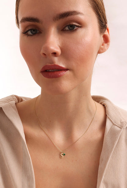 May include: A gold chain necklace with a small gold letter 'S' charm and a green gemstone accent.