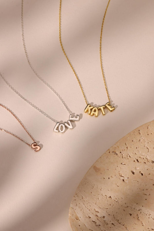 May include: A collection of delicate necklaces with pendant letters and words. The necklaces are in gold, silver, and rose gold. One necklace spells "LOVE", another "KATE", and a third features the letter "S".