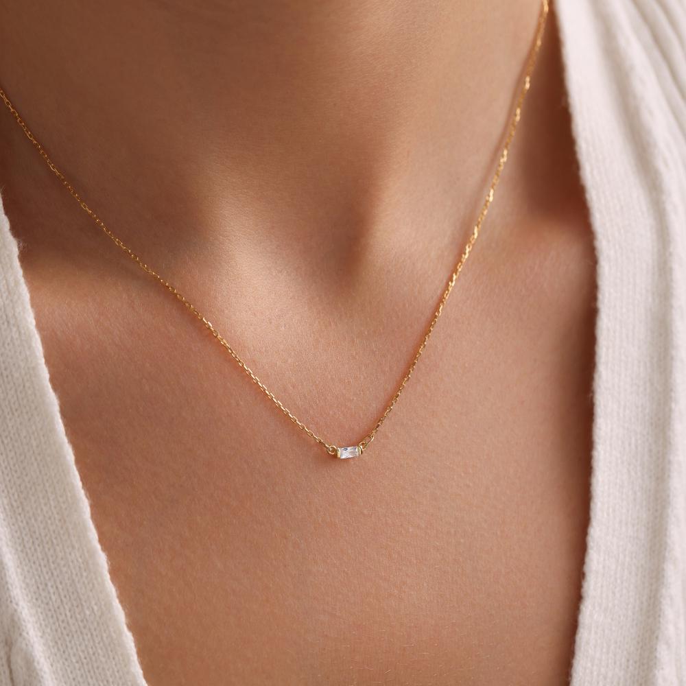 May include: A delicate gold chain necklace with a single, small, rectangular-shaped clear gemstone pendant.