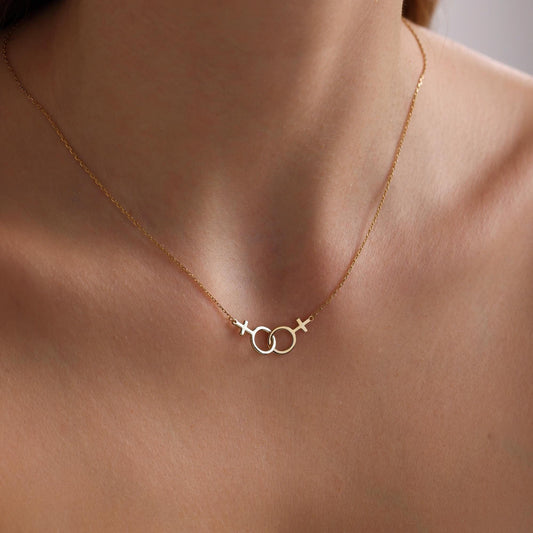 May include: A gold necklace with a delicate chain and a pendant featuring two interlocking circles with a cross at the top of each circle.