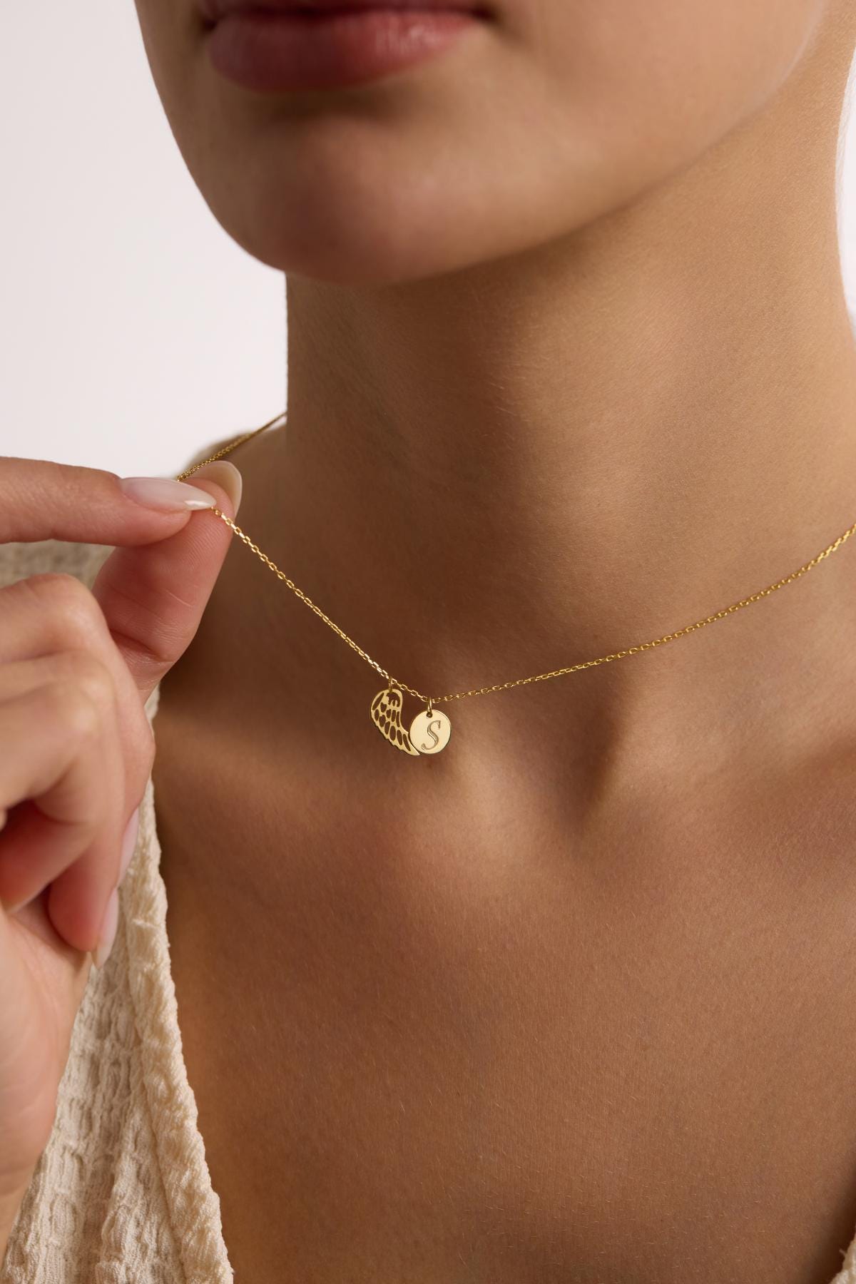 May include: A gold chain necklace with a delicate angel wing charm and a small round charm with the letter 'S' engraved on it.