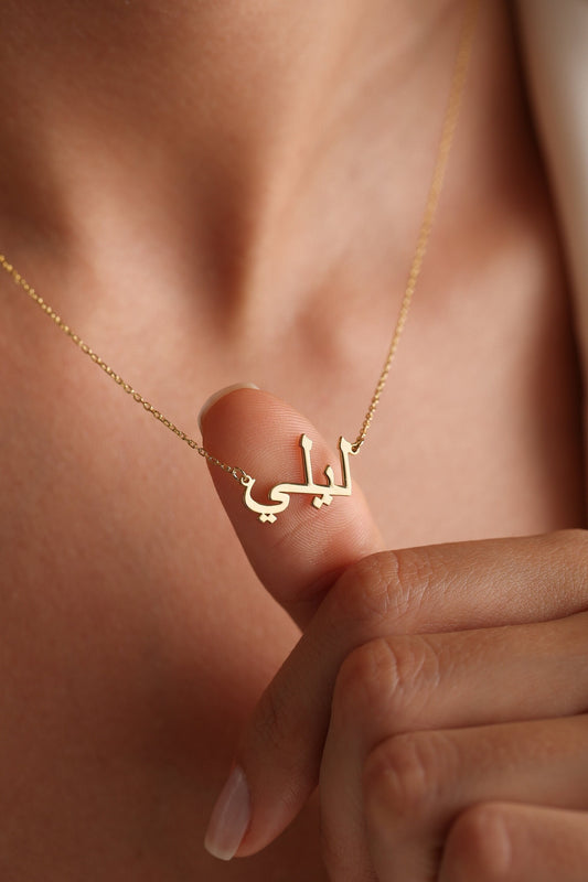 May include: A gold necklace with a delicate chain and a pendant featuring the Arabic word "Lali" in a simple, modern font.