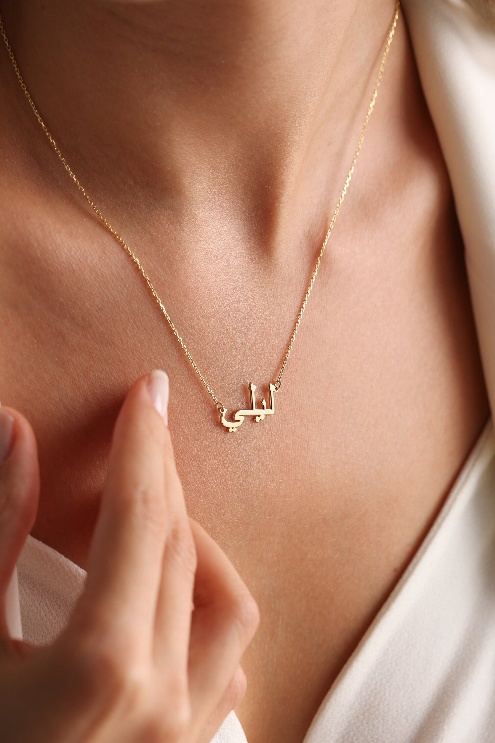 May include: A gold necklace with a delicate chain and a pendant featuring the Arabic word "Latifa" in a simple, elegant font.