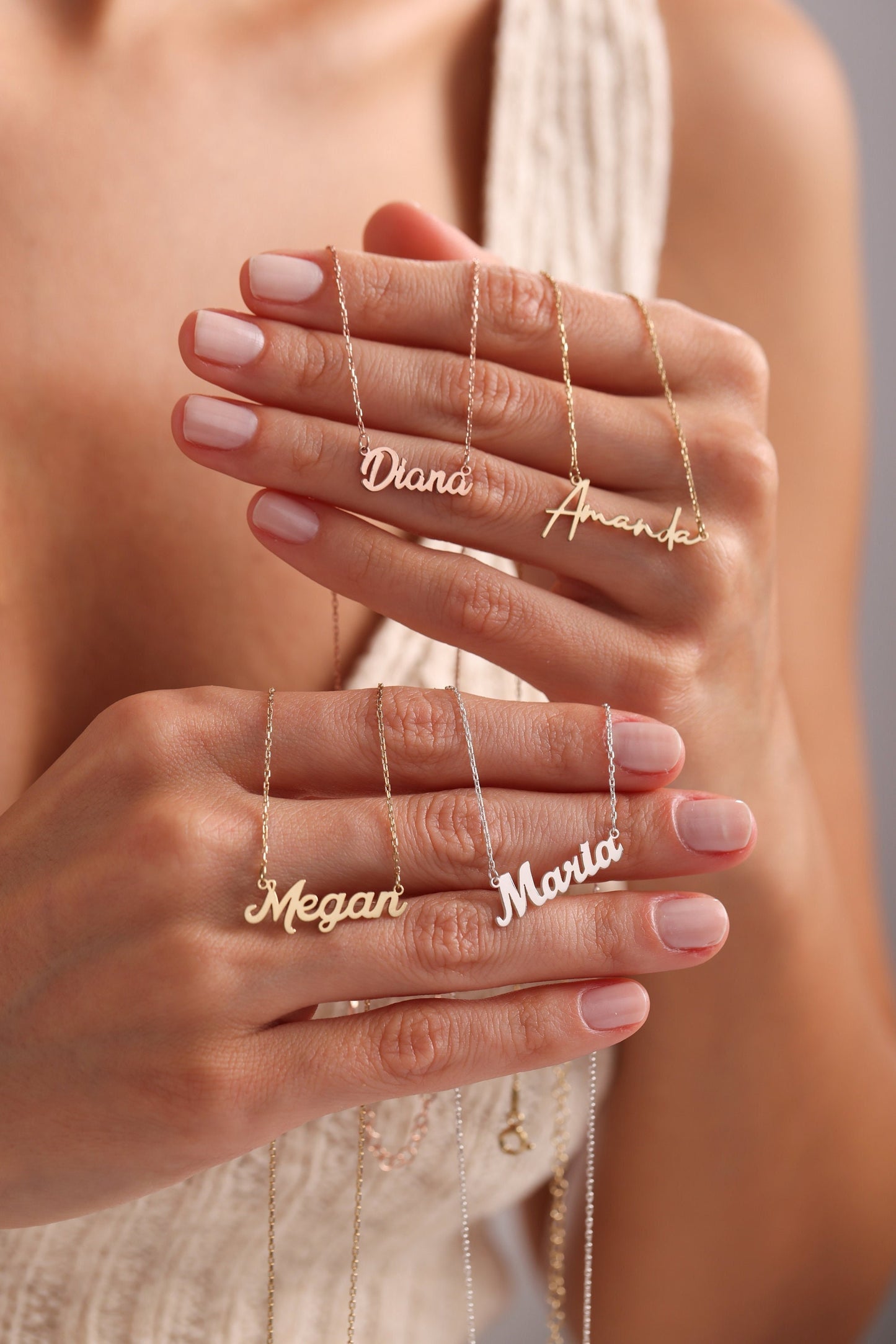 May include: Gold and silver name necklaces with delicate chain. The names "Diana", "Amanda", "Megan", and "Maria" are displayed in a cursive font. The necklaces are held up by a person.