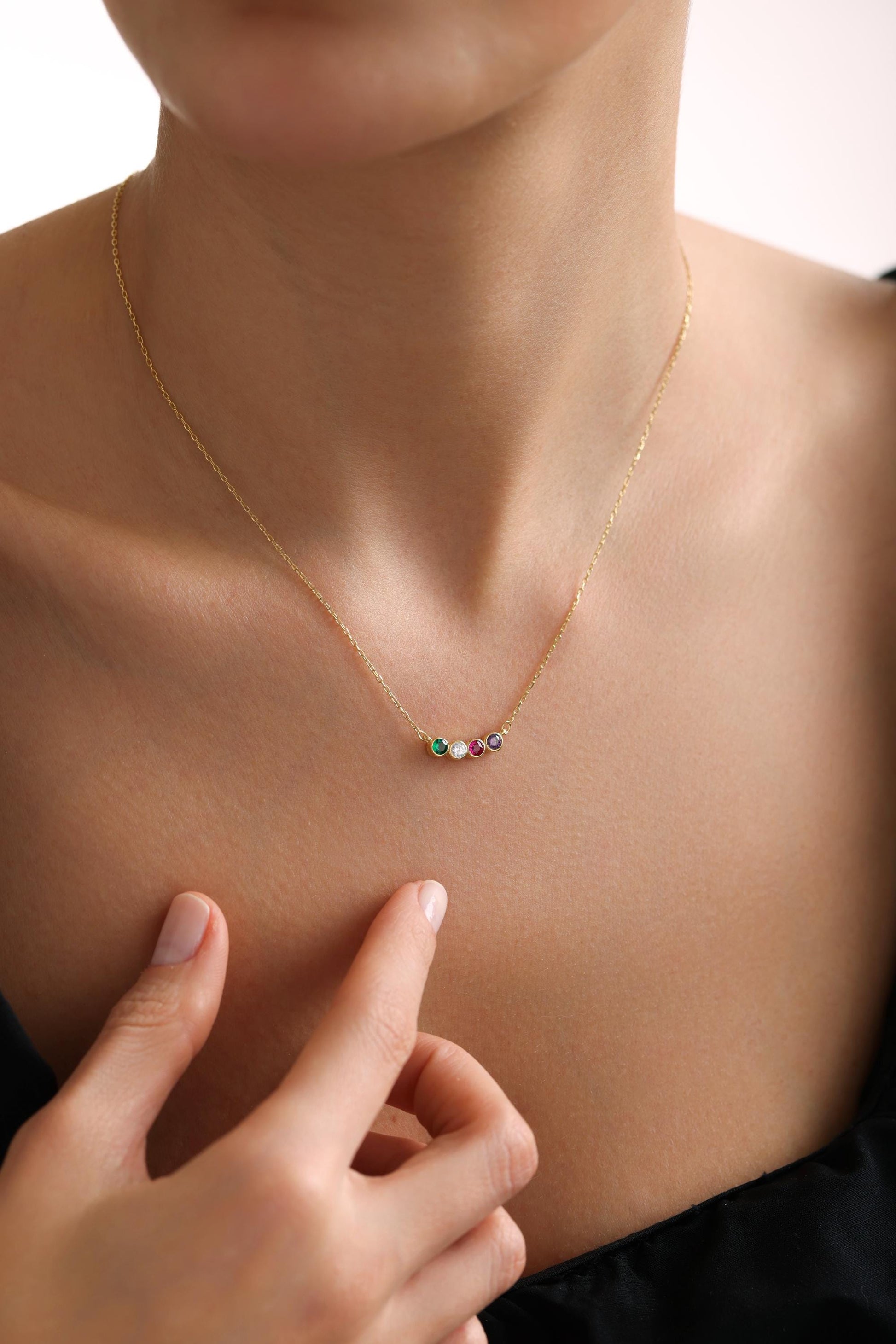 May include: A gold chain necklace with five small gemstones in a row. The gemstones are green, red, white, and purple.