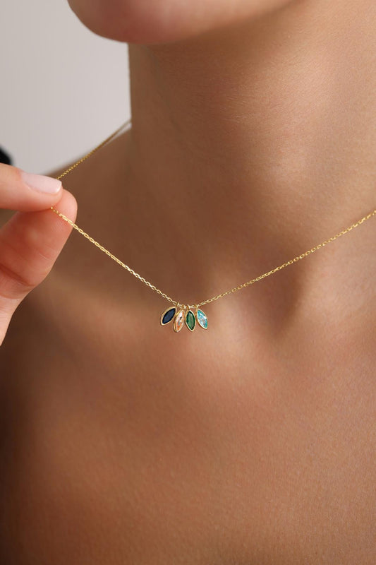 May include: A delicate gold necklace featuring five colorful gemstone pendants. The gemstones are in shades of blue, green, and peach. The necklace is being held by a person.