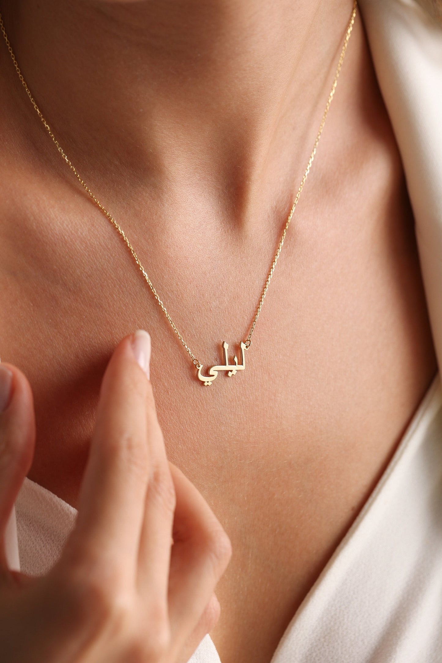 May include: A gold necklace with a delicate chain and a pendant featuring the Arabic word "Latifa" in a simple, elegant font.