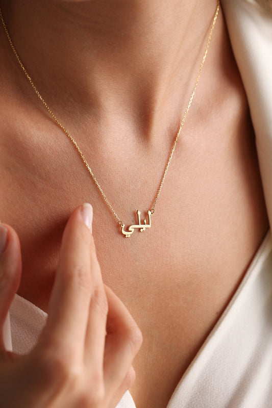 May include: A gold necklace with a delicate chain and a pendant featuring the Arabic word "Latifa" in a simple, elegant font.